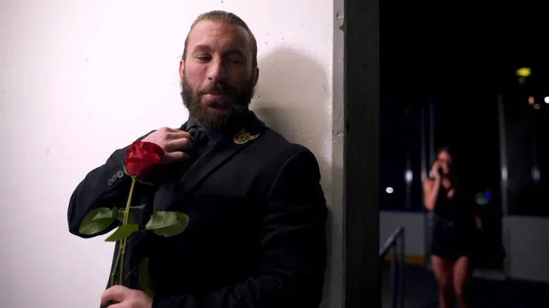 John Skyler with a rose in his hand while Mila Moore talks on the phone in the background